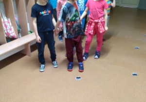 Dzieci w parach idą po śladach misia przyklejonych na podłodze holu przedszkola